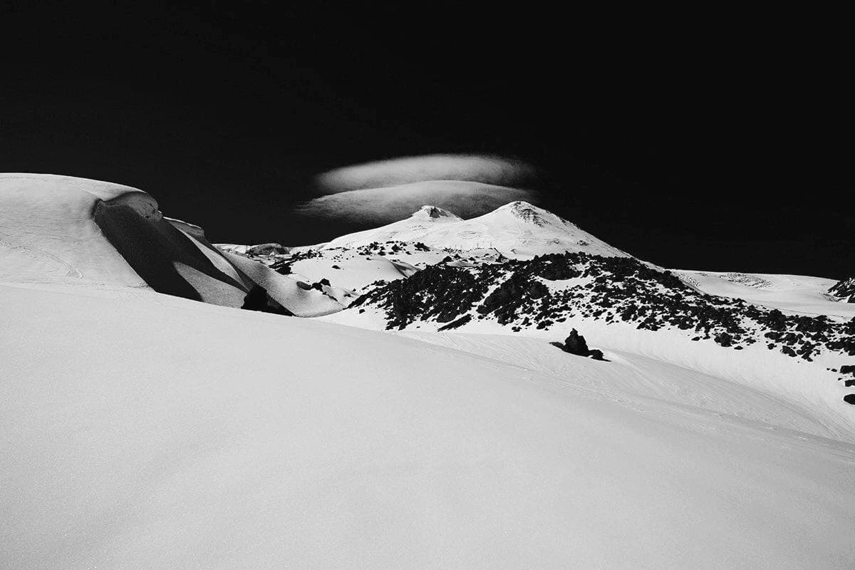 A lone mountain summit at dusk, lit from below by cloud